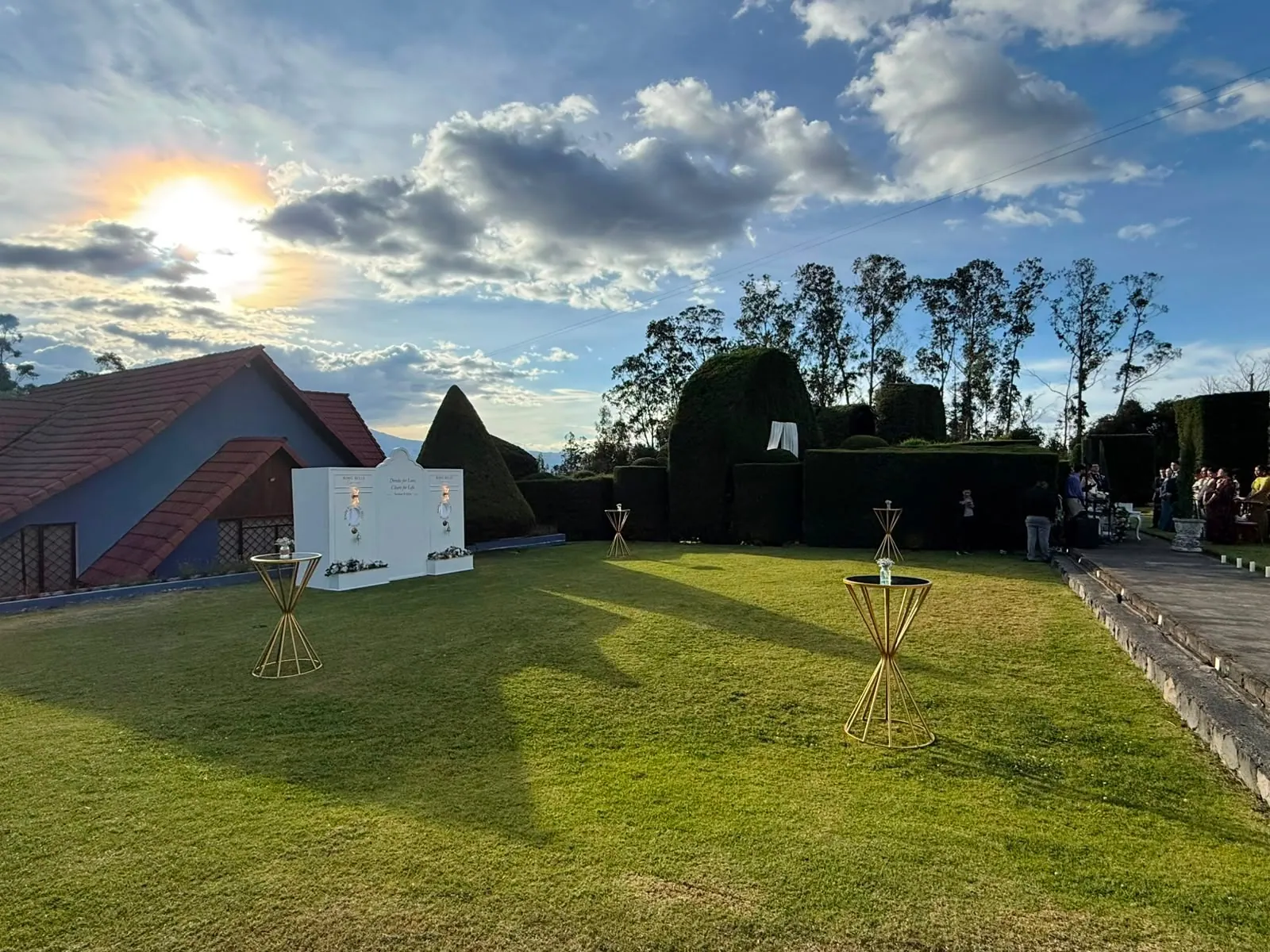 Vista general del jardín de la Quinta Las Tres Marías al atardecer, con la fachada de la propiedad, jardines topiarios y mesas altas para cóctel sobre el césped