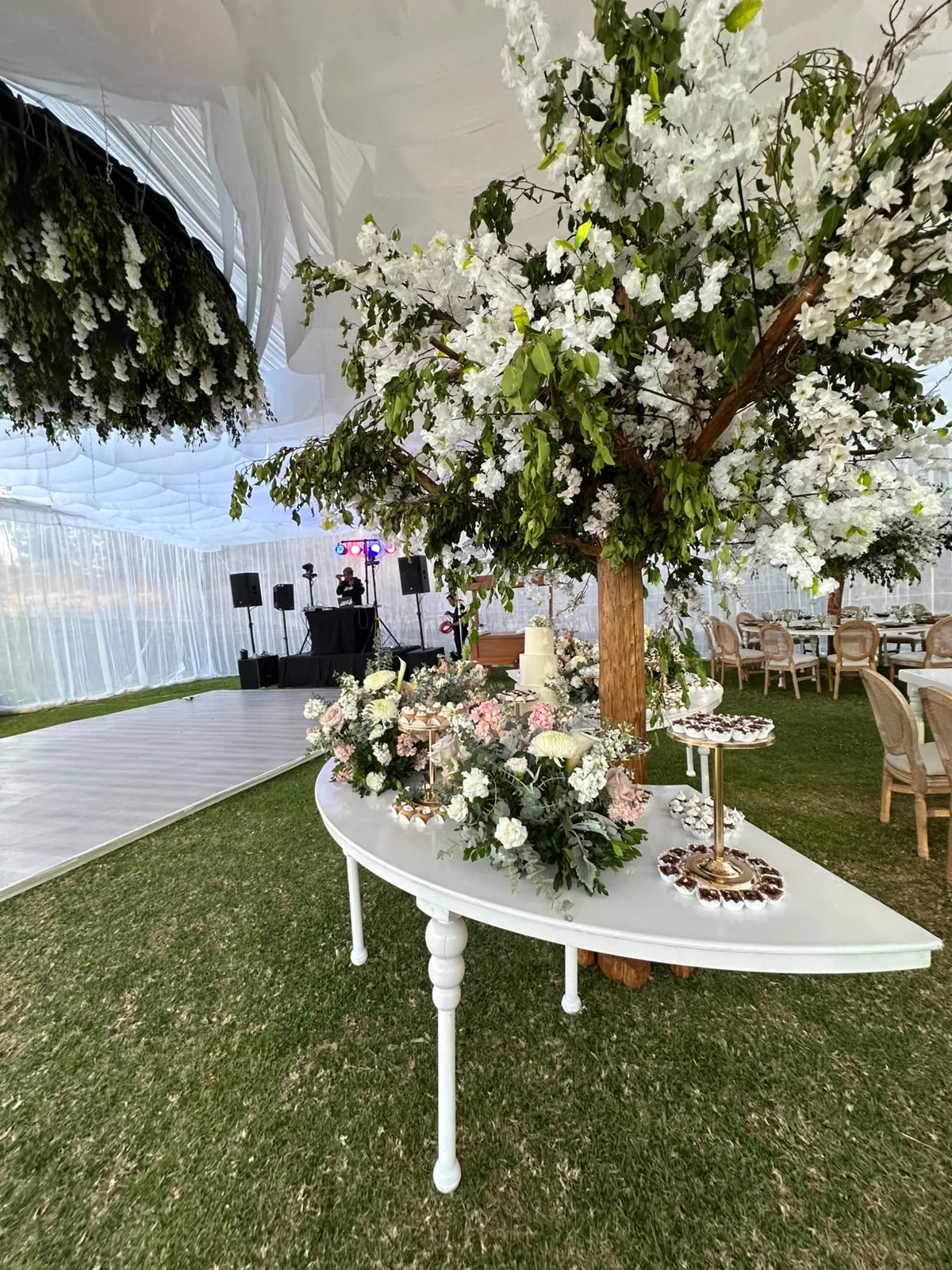 Mesa de dulces curva con arreglos de rosas y un árbol de flores blancas junto a las mesas