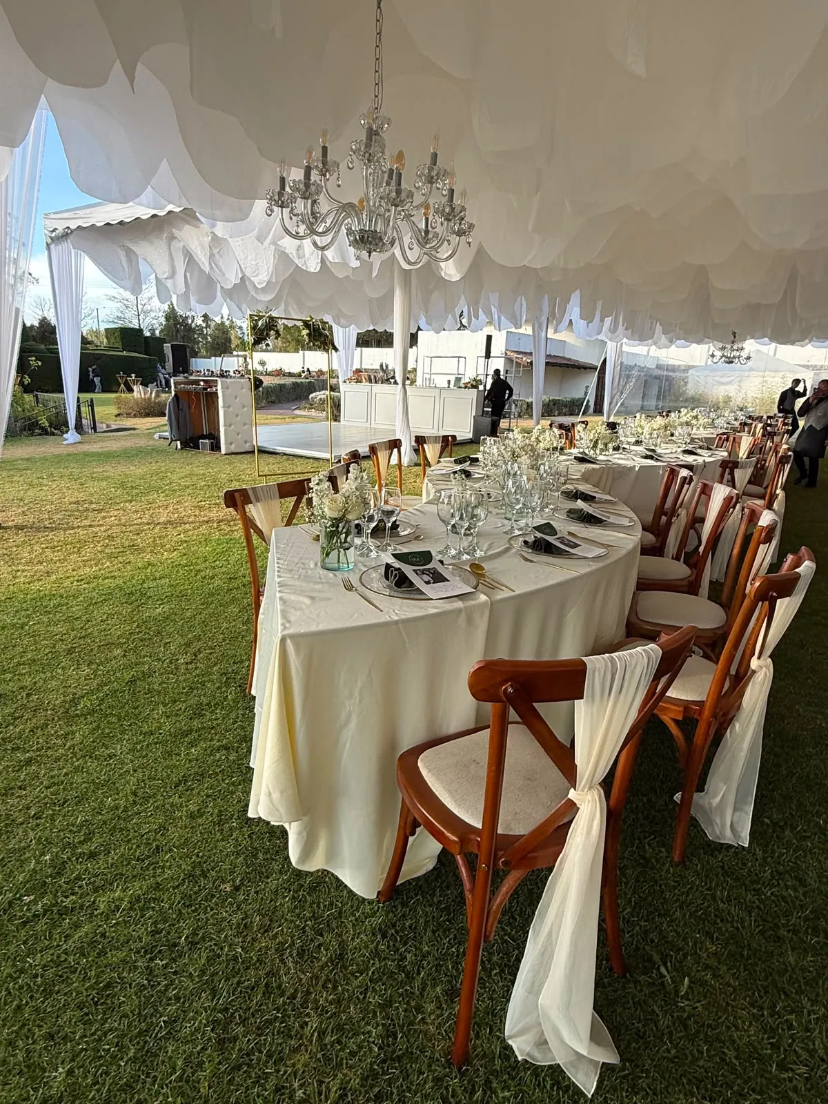 Mesa imperial vestida en marfil con sillas de madera y lazos de tela, bajo un candelabro